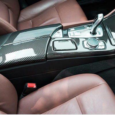 Imagine de interior BMW F10 cu protecție de carbon pe cotieră și tunel central. Reflexii elegante, look sportiv, finisaj negru lucios.