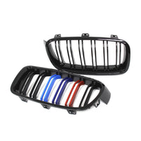 Imagine cu o grilă dublu rinichi pentru BMW Seria 3 F30/F31 (2012–2018), realizată din plastic ABS negru lucios, cu detalii colorate în stil M Performance (albastru deschis, albastru închis și roșu). Fotografie de produs pe fundal alb, unghi frontal și lateral, ce evidențiază designul sportiv și calitatea materialelor.