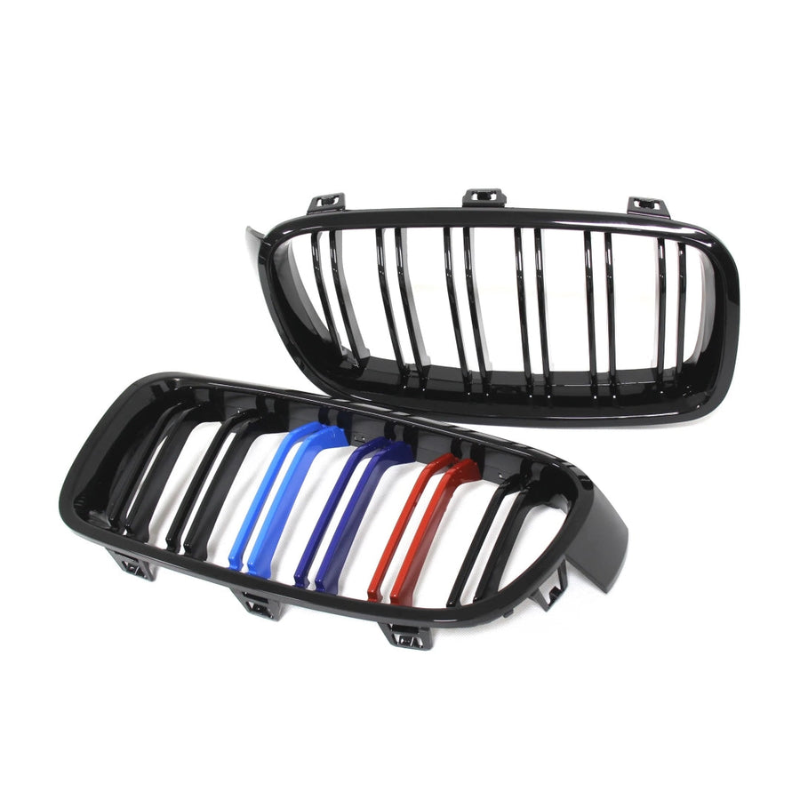 Imagine cu o grilă dublu rinichi pentru BMW Seria 3 F30/F31 (2012–2018), realizată din plastic ABS negru lucios, cu detalii colorate în stil M Performance (albastru deschis, albastru închis și roșu). Fotografie de produs pe fundal alb, unghi frontal și lateral, ce evidențiază designul sportiv și calitatea materialelor.