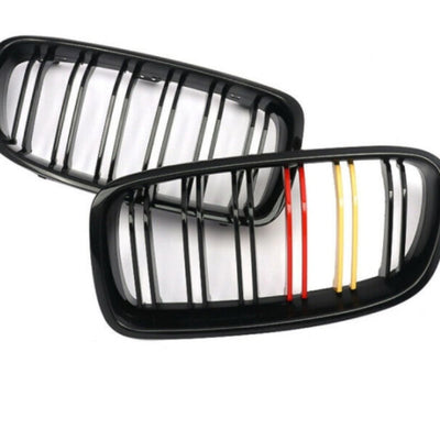 Grile duble BMW F10/F11 M Performance, unghi de prezentare superior, cu lamele negre și inserții galben-roșu pentru aspect sportiv.